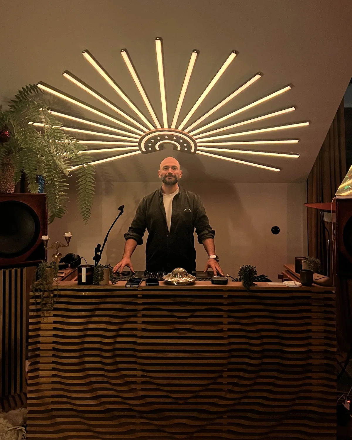 Kayvan, curator and guide of Dalliance, behind his DJ booth under a sunburst light